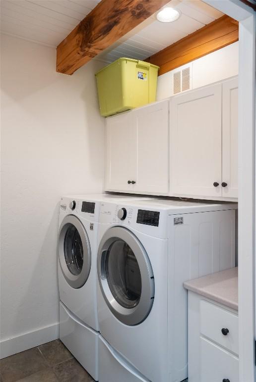 clothes washing area featuring visible vents, dark tile patterned flooring, washer and dryer, cabinet space, and baseboards