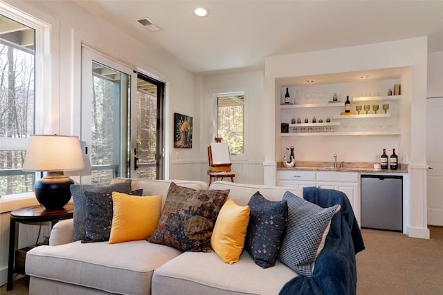 living area with visible vents, a healthy amount of sunlight, wet bar, and light colored carpet