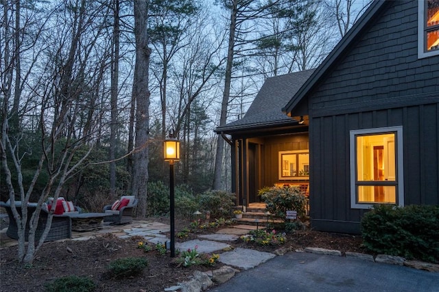 entrance to property with board and batten siding, a shingled roof, and a patio area