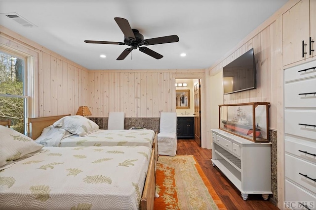 bedroom featuring ceiling fan, connected bathroom, wood walls, and dark hardwood / wood-style flooring