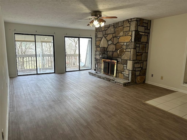 unfurnished living room with baseboards, a ceiling fan, wood finished floors, a textured ceiling, and a stone fireplace