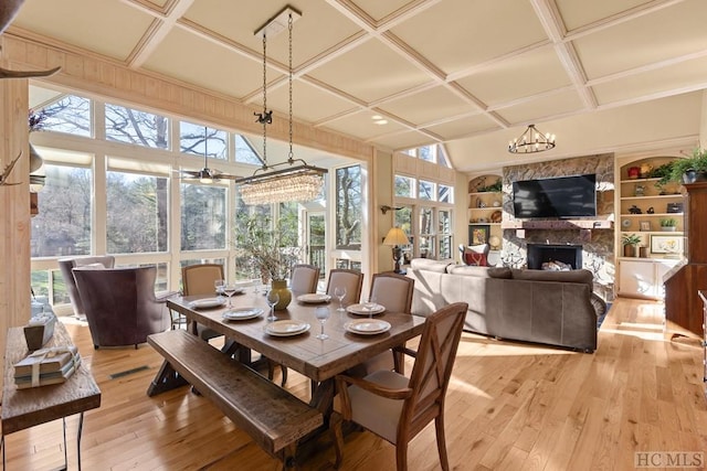 dining area featuring built in shelves, light hardwood / wood-style floors, a chandelier, coffered ceiling, and a fireplace