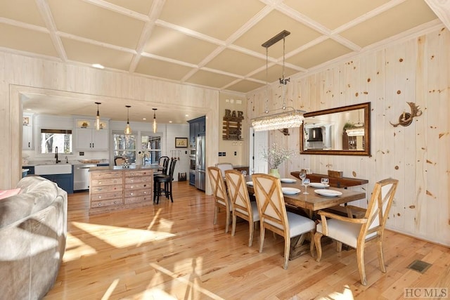 dining area featuring light hardwood / wood-style flooring, sink, wood walls, and coffered ceiling