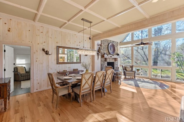 dining space with coffered ceiling, a stone fireplace, and light wood-type flooring