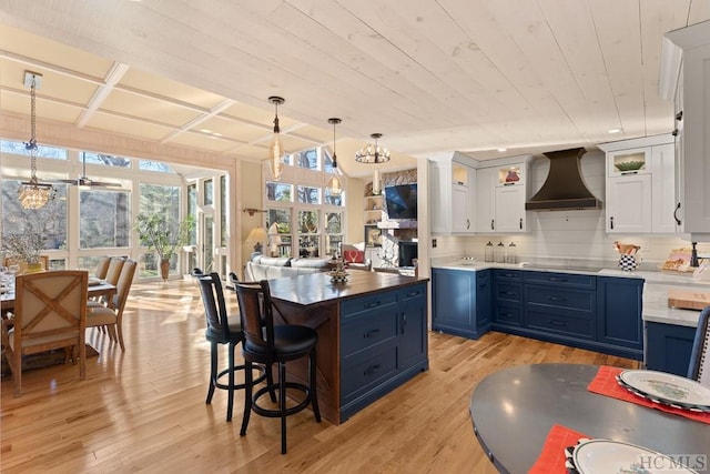 kitchen with blue cabinets, pendant lighting, wall chimney range hood, light hardwood / wood-style floors, and white cabinets