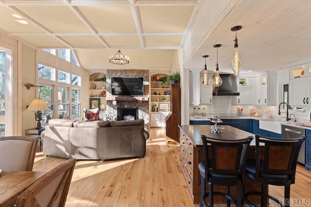 interior space featuring white cabinetry, hanging light fixtures, blue cabinets, a kitchen bar, and wall chimney exhaust hood