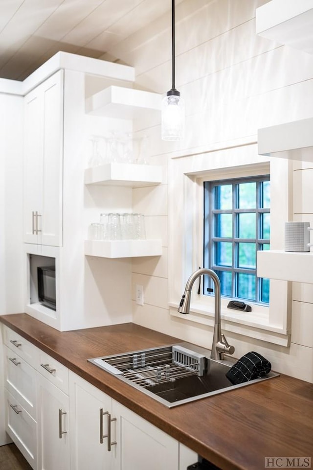 kitchen featuring pendant lighting, white cabinetry, butcher block counters, and sink