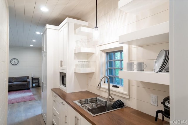 kitchen featuring sink, butcher block counters, hanging light fixtures, white cabinetry, and wood-type flooring