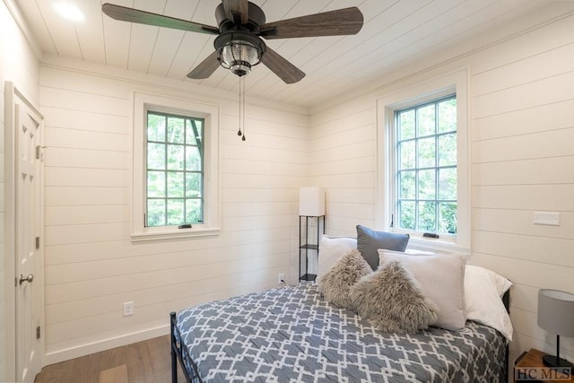 bedroom featuring wood-type flooring, wooden walls, and ceiling fan