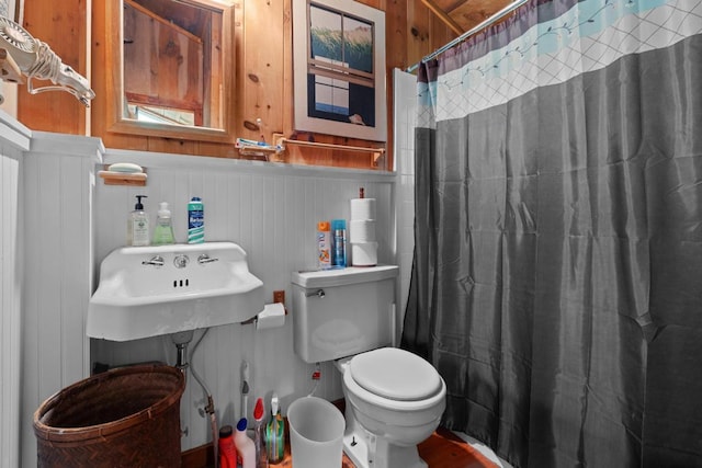bathroom with toilet, a sink, curtained shower, and a wainscoted wall