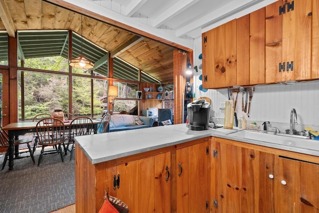 kitchen featuring a sink, light countertops, brown cabinetry, a peninsula, and vaulted ceiling