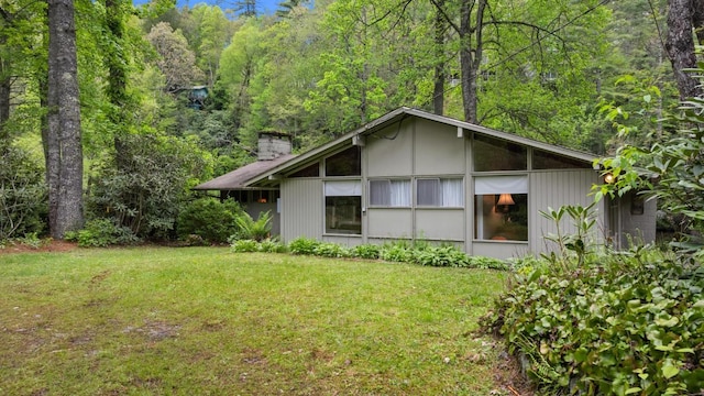 view of property exterior featuring a yard, a chimney, and a view of trees