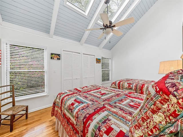 bedroom featuring light wood-style flooring, a skylight, beamed ceiling, a ceiling fan, and baseboards