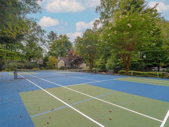 view of tennis court with fence, community basketball court, and view of scattered trees