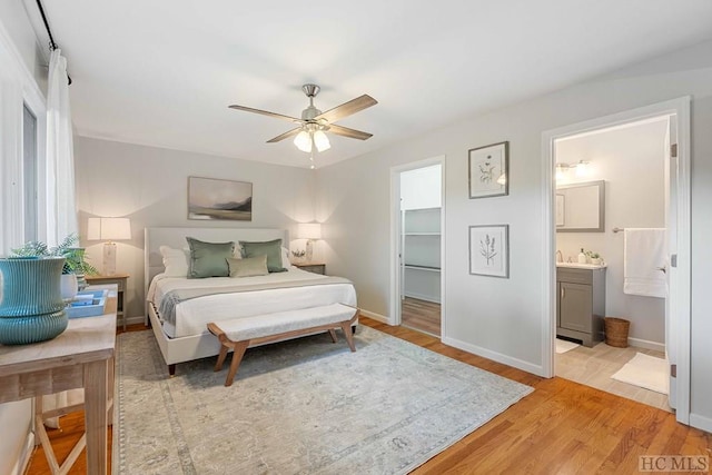 bedroom with connected bathroom, a walk in closet, a closet, ceiling fan, and light hardwood / wood-style floors