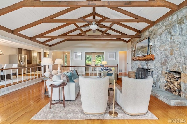 living room featuring high vaulted ceiling, beam ceiling, a stone fireplace, and light hardwood / wood-style floors