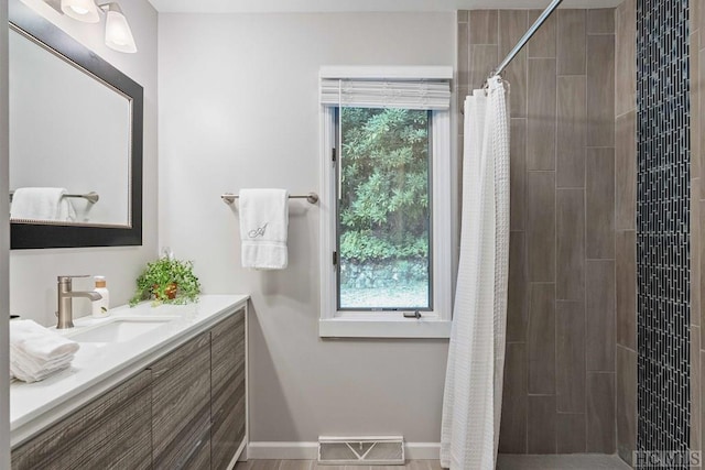 full bath featuring baseboards, visible vents, tiled shower, and vanity