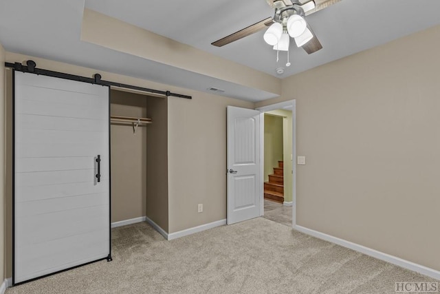 unfurnished bedroom featuring ceiling fan, a barn door, light carpet, and a closet