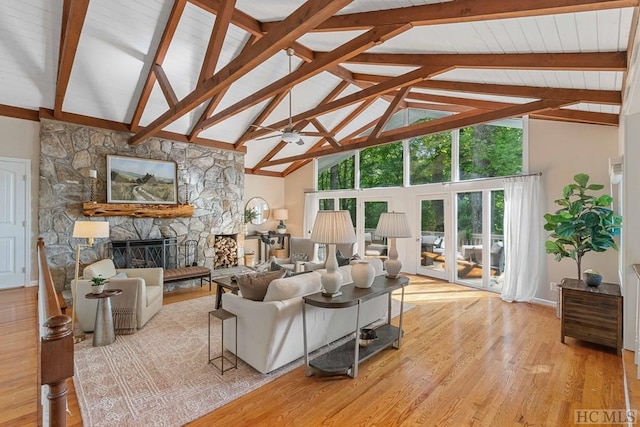 living room featuring ceiling fan, high vaulted ceiling, a stone fireplace, beamed ceiling, and light wood-type flooring