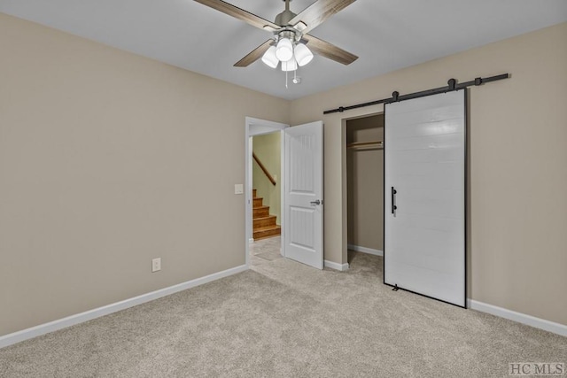 unfurnished bedroom featuring a barn door, light colored carpet, ceiling fan, and a closet