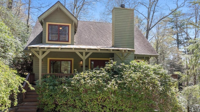 view of front facade featuring roof with shingles, a chimney, and a porch