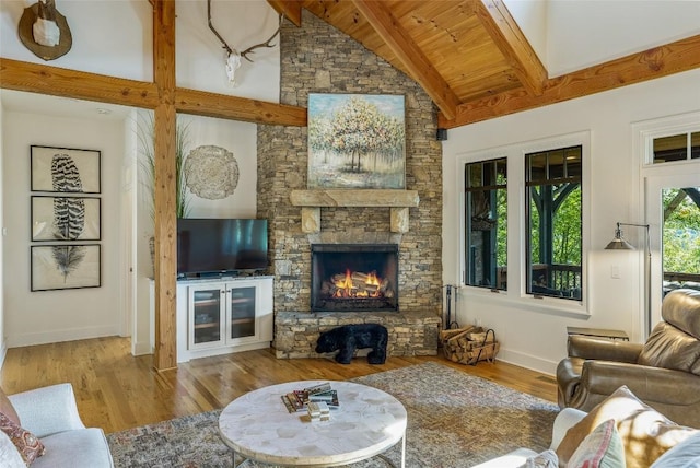 living room featuring beamed ceiling, light hardwood / wood-style flooring, a stone fireplace, and high vaulted ceiling