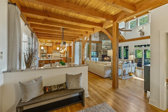 living room with light wood-type flooring, beam ceiling, a stone fireplace, wood ceiling, and a notable chandelier