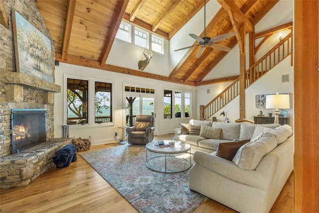 living room featuring beamed ceiling, a stone fireplace, ceiling fan, light wood-type flooring, and high vaulted ceiling