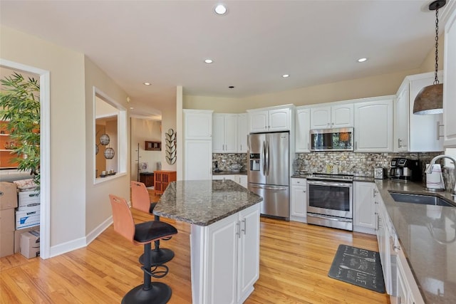 kitchen featuring stainless steel appliances, a sink, white cabinets, and a center island