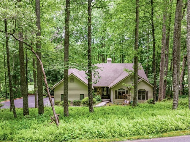 view of front of house with roof with shingles, a chimney, and a wooded view