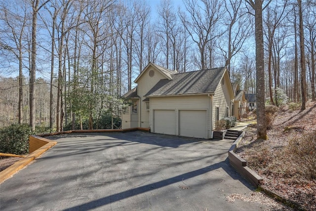 view of side of property featuring a garage, aphalt driveway, and a shingled roof