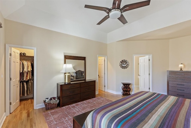 bedroom featuring a ceiling fan, a walk in closet, baseboards, and wood finished floors