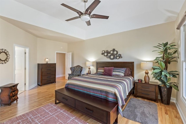 bedroom featuring ceiling fan, a tray ceiling, wood finished floors, and baseboards