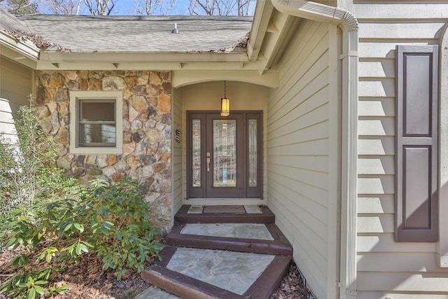 doorway to property featuring stone siding and roof with shingles