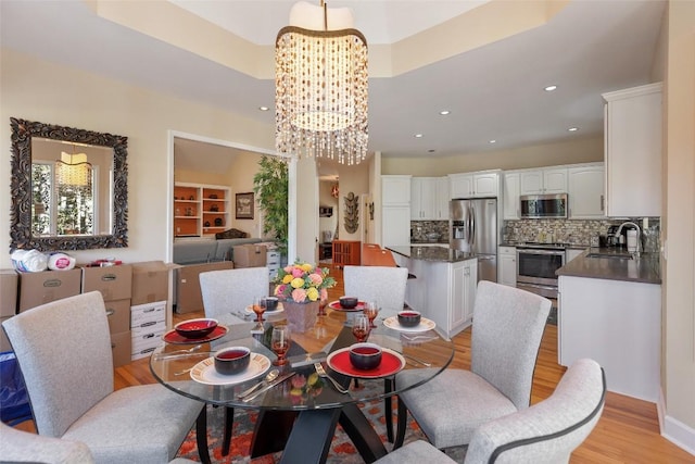 dining room with light wood finished floors, a raised ceiling, a notable chandelier, and recessed lighting