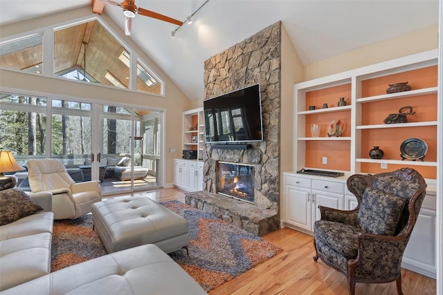 living area with high vaulted ceiling, rail lighting, a fireplace, and light wood-style flooring