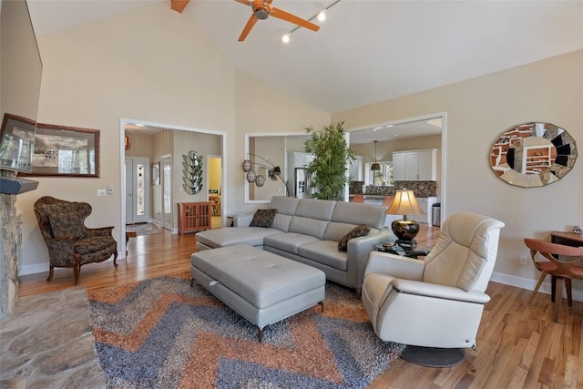 living area featuring ceiling fan, high vaulted ceiling, light wood-type flooring, and baseboards