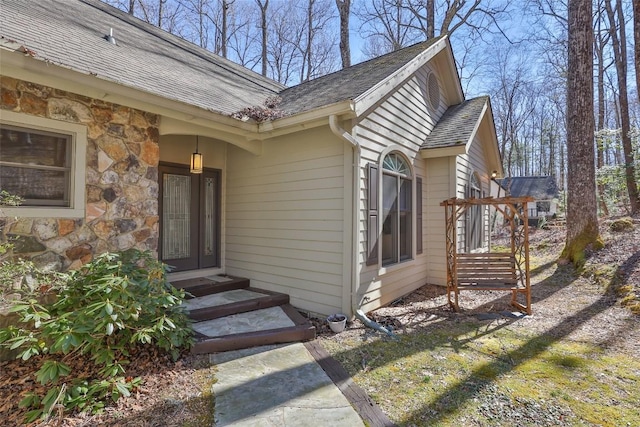 view of exterior entry with a shingled roof and stone siding