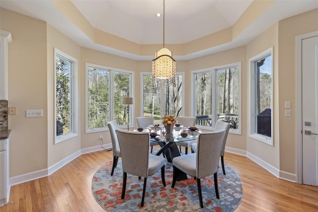 dining area featuring light wood-type flooring, a tray ceiling, a wealth of natural light, and baseboards