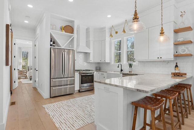 kitchen with a peninsula, stainless steel appliances, wall chimney range hood, and open shelves