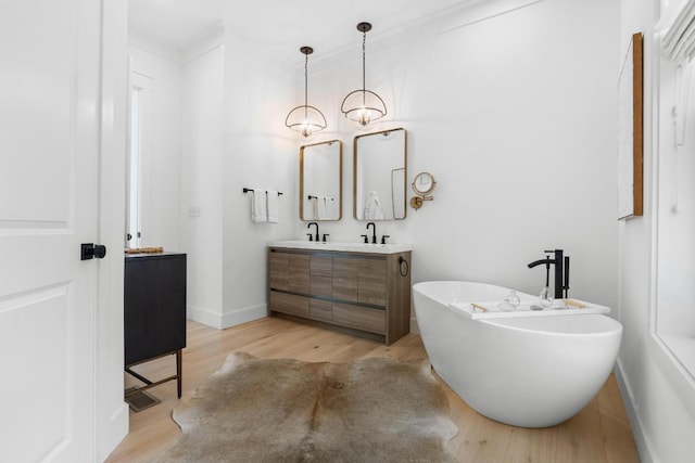 full bath with double vanity, a freestanding tub, wood finished floors, and baseboards