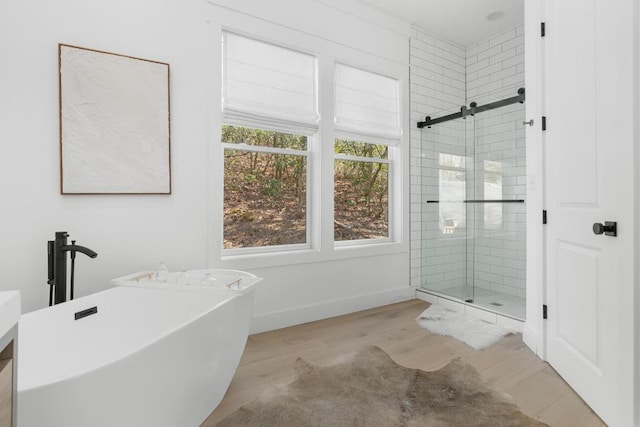 bathroom with a freestanding tub, baseboards, wood finished floors, and a shower stall