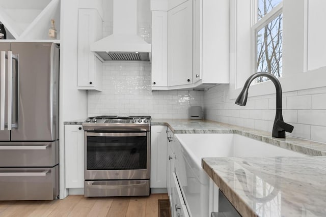 kitchen featuring appliances with stainless steel finishes, light wood-style floors, custom exhaust hood, white cabinetry, and a sink