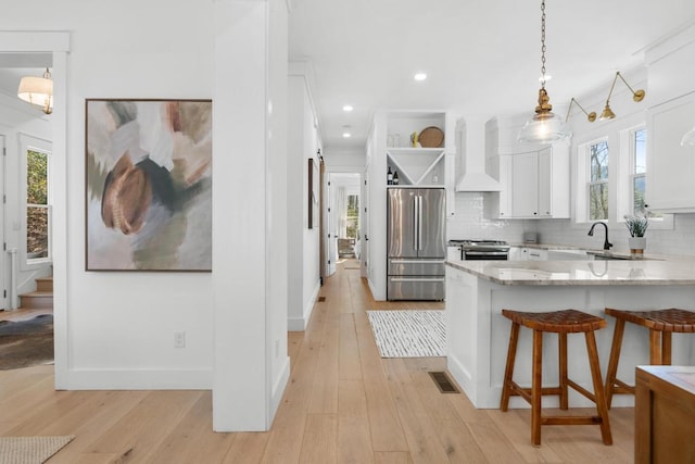 kitchen featuring open shelves, appliances with stainless steel finishes, wall chimney exhaust hood, white cabinets, and decorative backsplash