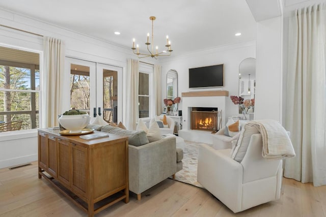 living area with visible vents, light wood-style flooring, ornamental molding, a warm lit fireplace, and an inviting chandelier