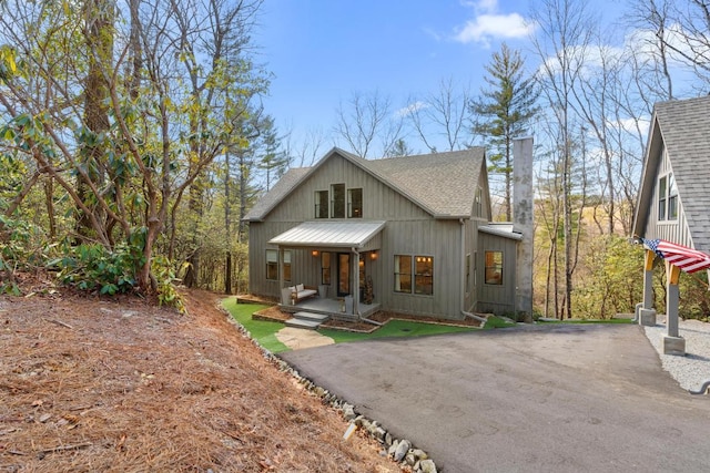 view of front of home featuring aphalt driveway, covered porch, a shingled roof, and metal roof