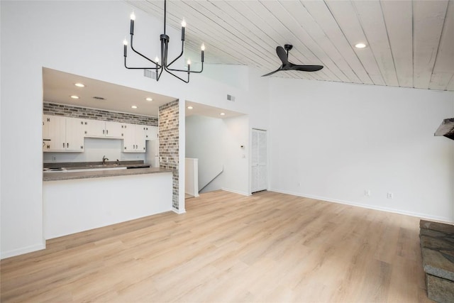 unfurnished living room with light wood-style flooring, a high ceiling, recessed lighting, a chandelier, and ceiling fan
