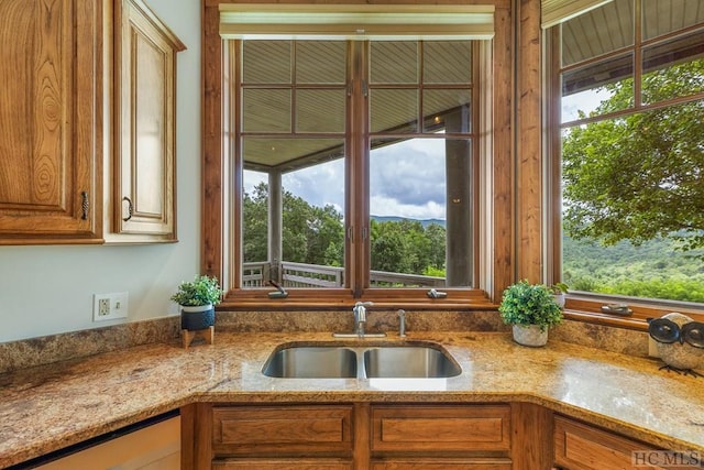 kitchen featuring dishwashing machine, a wealth of natural light, sink, and light stone counters