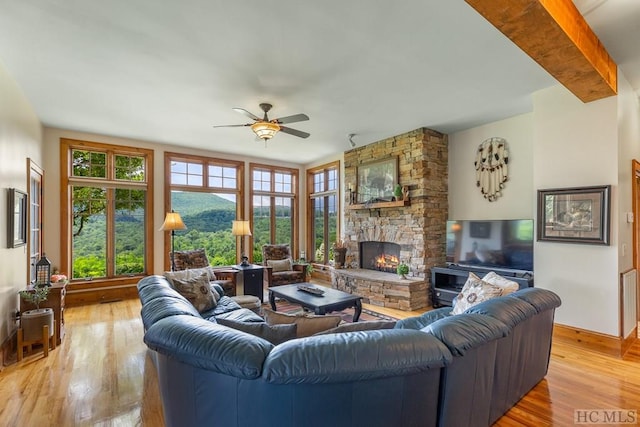 living room with ceiling fan, wood-type flooring, beamed ceiling, and a stone fireplace