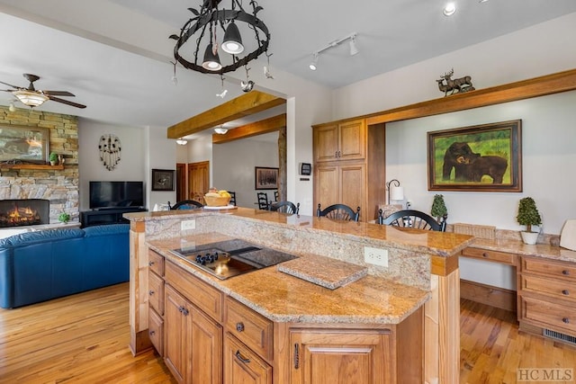 kitchen with a stone fireplace, light stone counters, a center island, black electric cooktop, and a kitchen breakfast bar